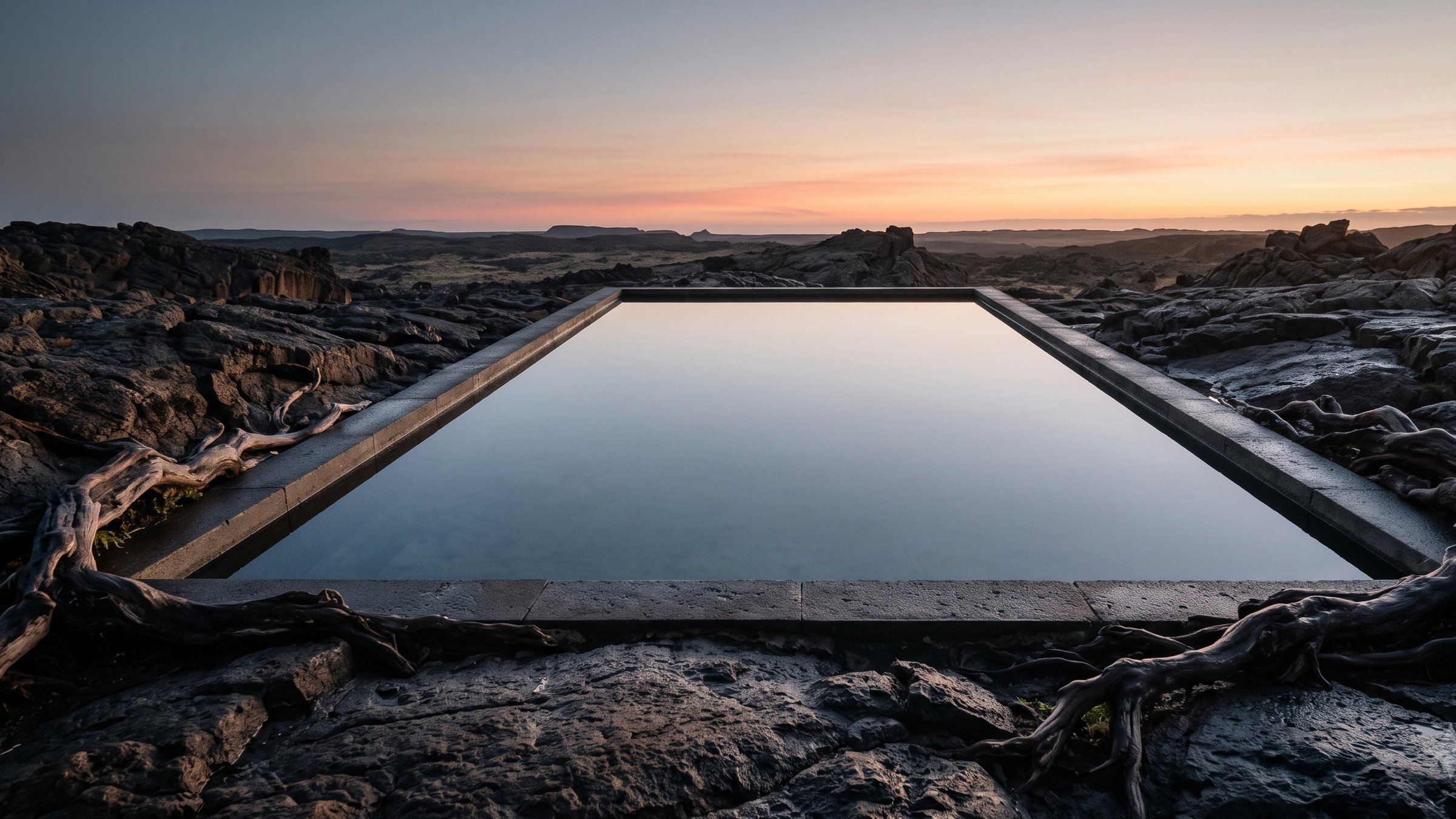 Dark volcanic bedrock holding a perfectly still rectangular reflecting pool of clear water, strong old roots gripping the rock at the edges, mirroring a slowly warming dawn sky without a single ripple.